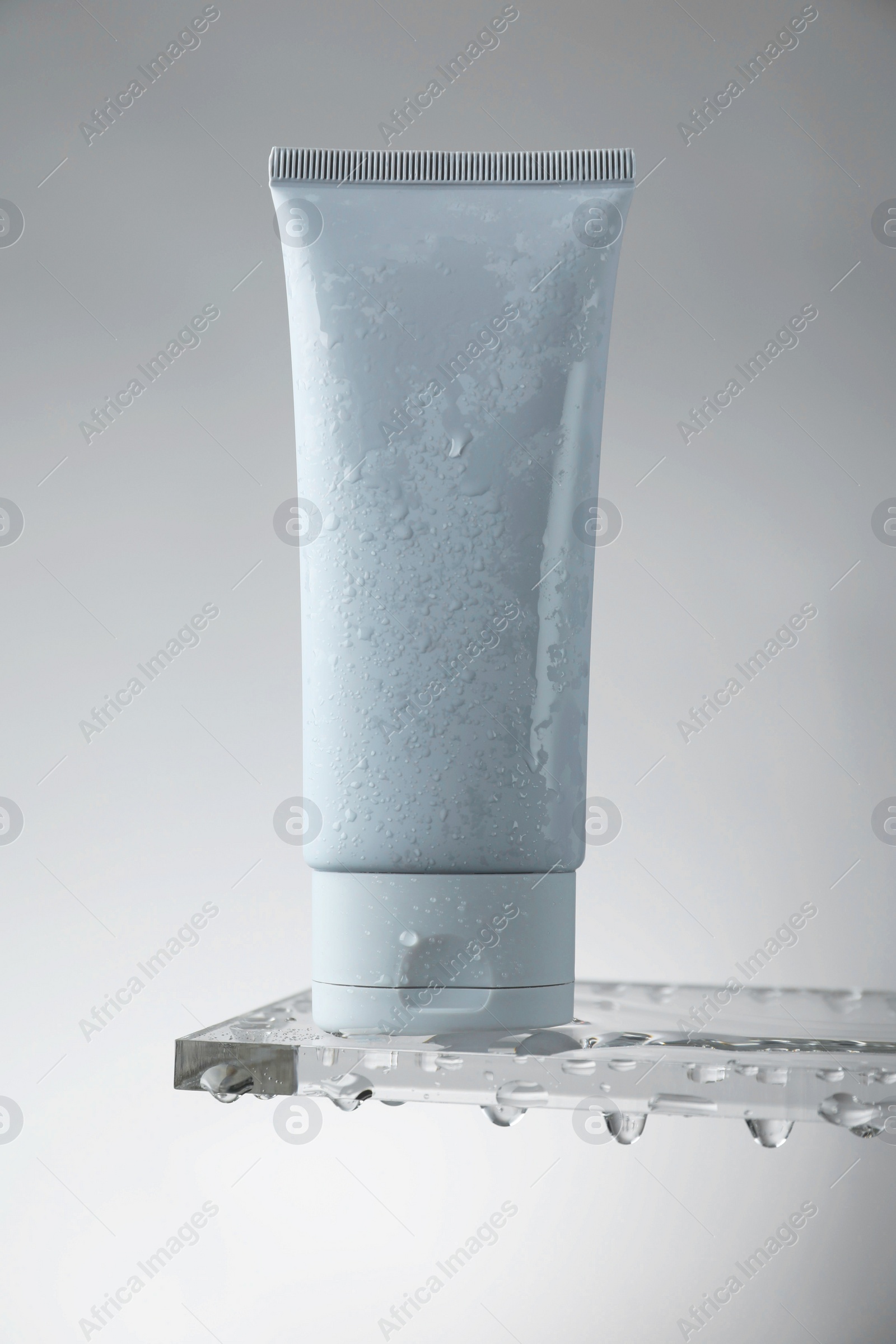 Photo of Moisturizing cream in tube on glass with water drops against grey background