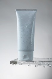 Moisturizing cream in tube on glass with water drops against grey background