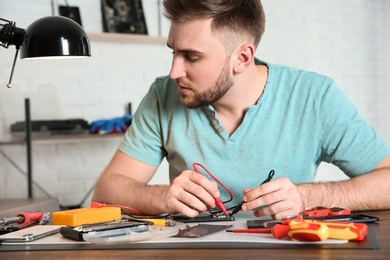 Technician checking mobile phone at table in repair shop