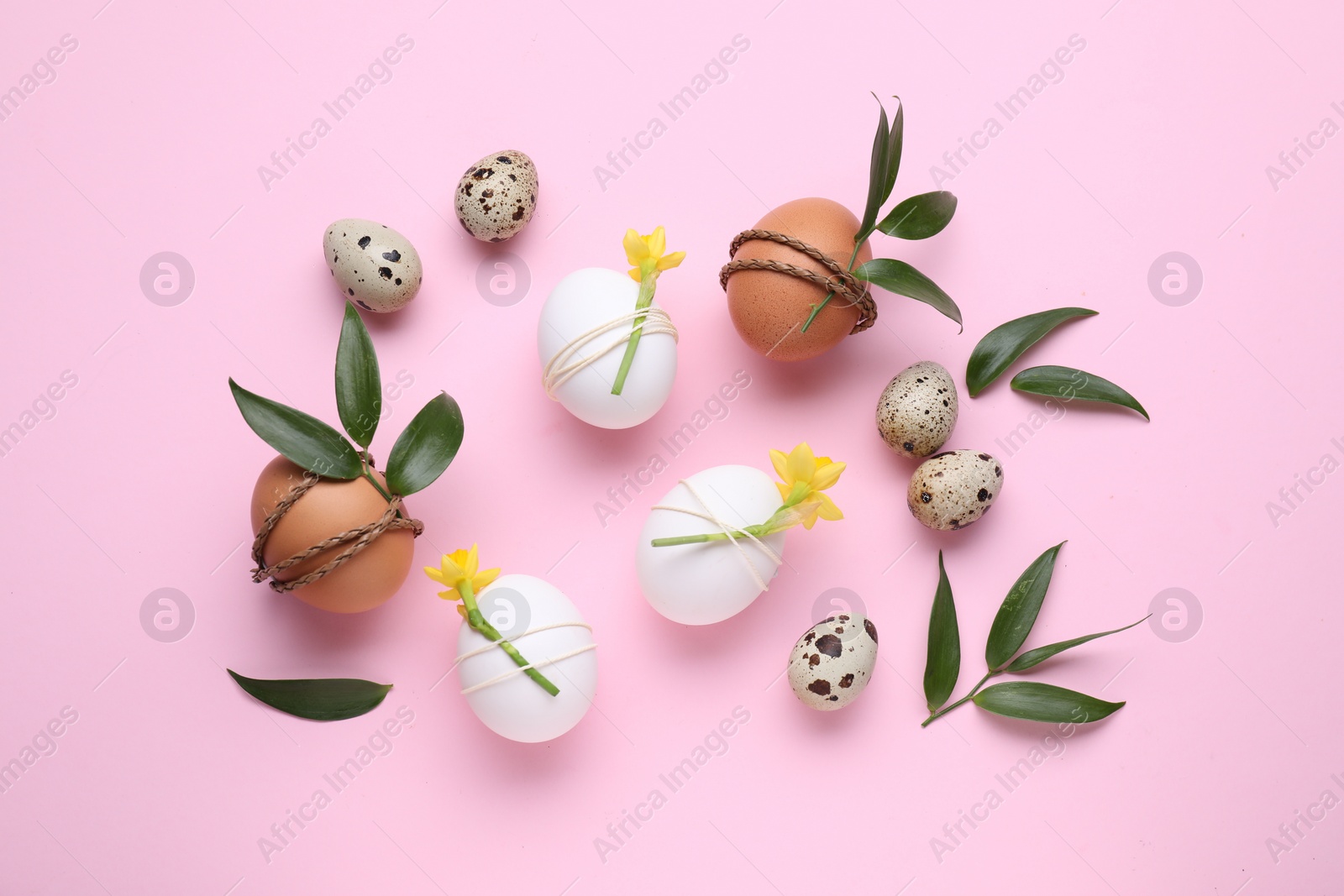 Photo of Easter eggs decorated with green leaves and flowers on pink background, flat lay