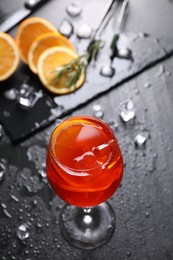 Glass of tasty Aperol spritz cocktail with orange slices and ice cubes on dark gray table, above view