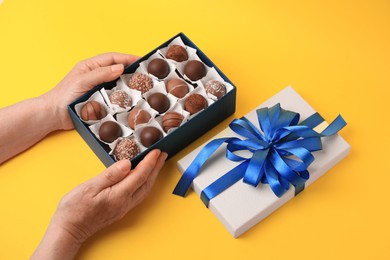 Photo of Woman with box of delicious chocolate candies on yellow background, closeup