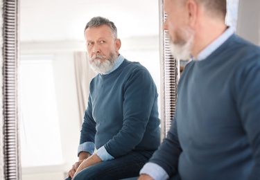 Photo of Mature man looking in mirror at home