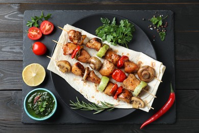 Delicious shish kebabs with vegetables served on black wooden table, top view