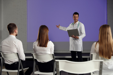 Photo of Male doctor with laptop giving lecture in conference room with projection screen