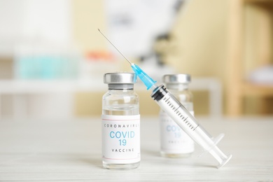 Photo of Vials with vaccine against Covid-19 and syringe on white table indoors