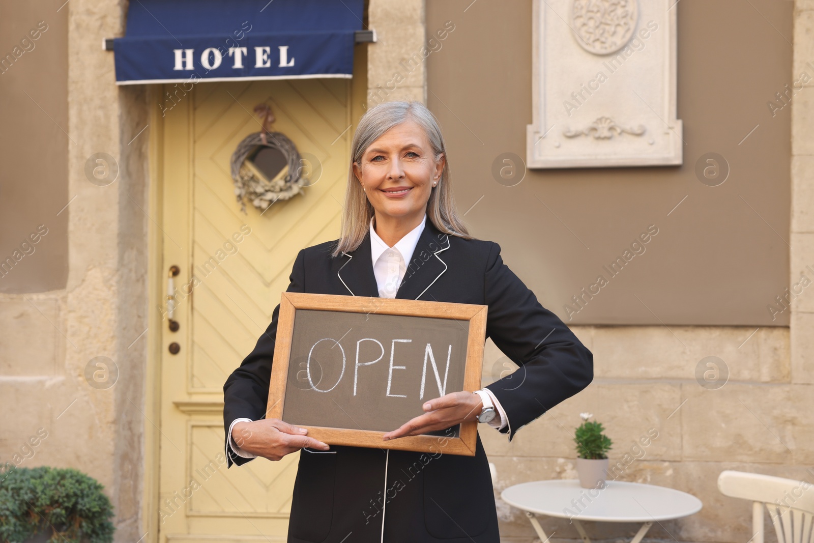 Photo of Happy business owner holding open sign near her hotel outdoors