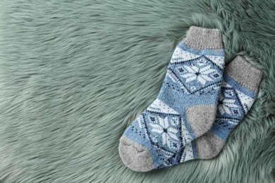 Photo of Knitted socks on grey faux fur, flat lay. Space for text