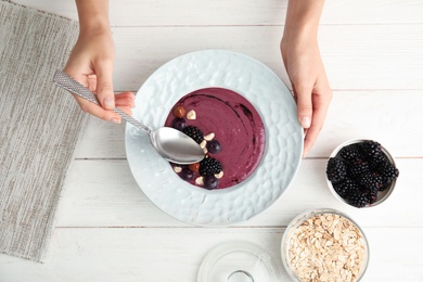 Woman eating tasty acai smoothie at table, closeup