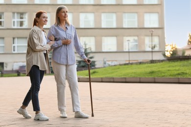 Photo of Senior lady with walking cane and young woman outdoors. Space for text