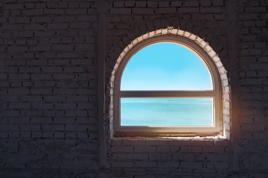 Beautiful sky and sea visible through old window in brick wall 
