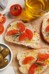 Photo of Tasty bruschettas with oil, tomatoes and rosemary on parchment paper, flat lay