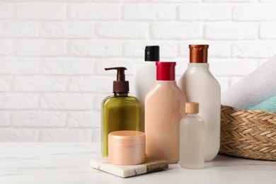 Shampoo bottles, hair mask, essential oil and towels on white marble table