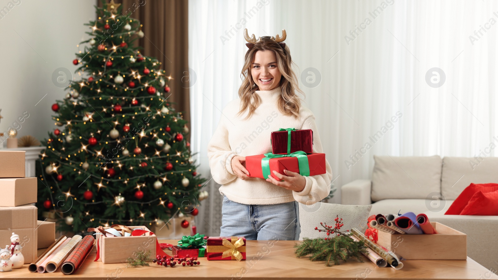 Photo of Young woman with beautifully wrapped Christmas gifts at home