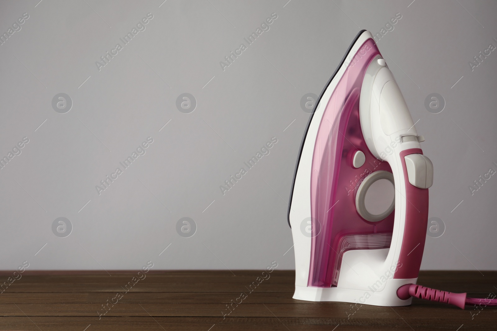 Photo of One modern iron on wooden table against light grey background, space for text. Home appliance