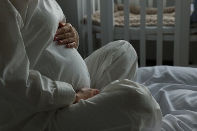 Pregnant woman in pajamas on bed at home, closeup
