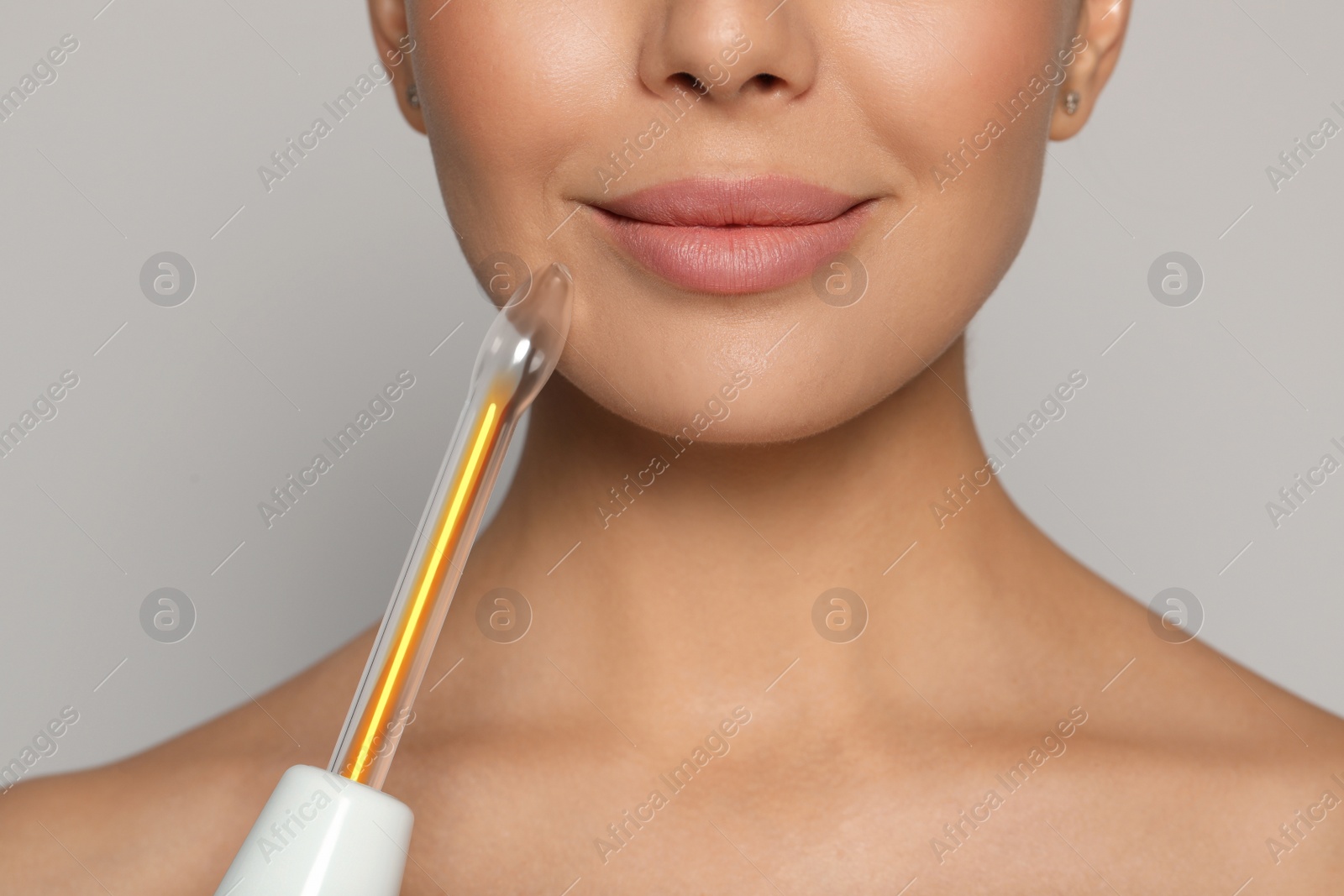 Photo of Woman using high frequency darsonval device on grey background, closeup