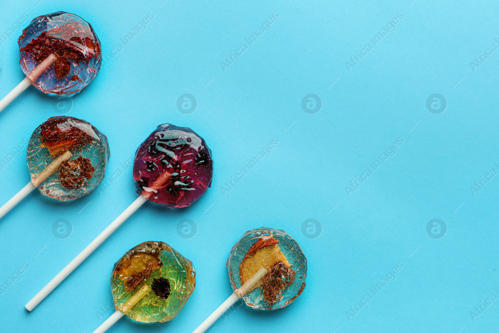 Photo of Sweet colorful lollipops with berries on light blue background, flat lay. Space for text