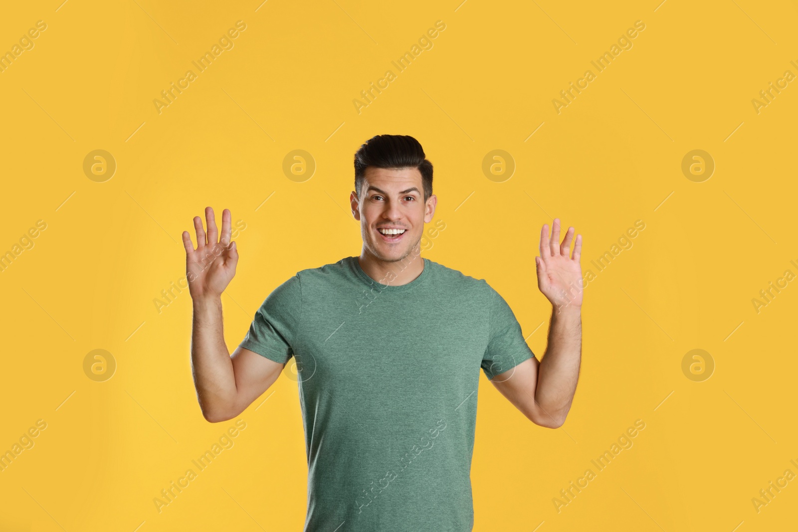 Photo of Cheerful man waving to say hello on yellow  background