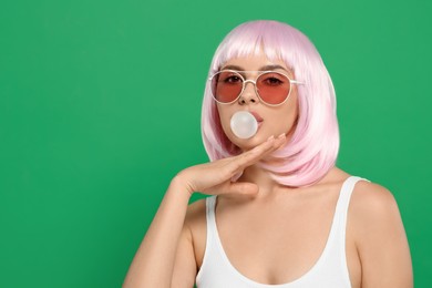 Photo of Beautiful woman in sunglasses blowing bubble gum on green background, space for text