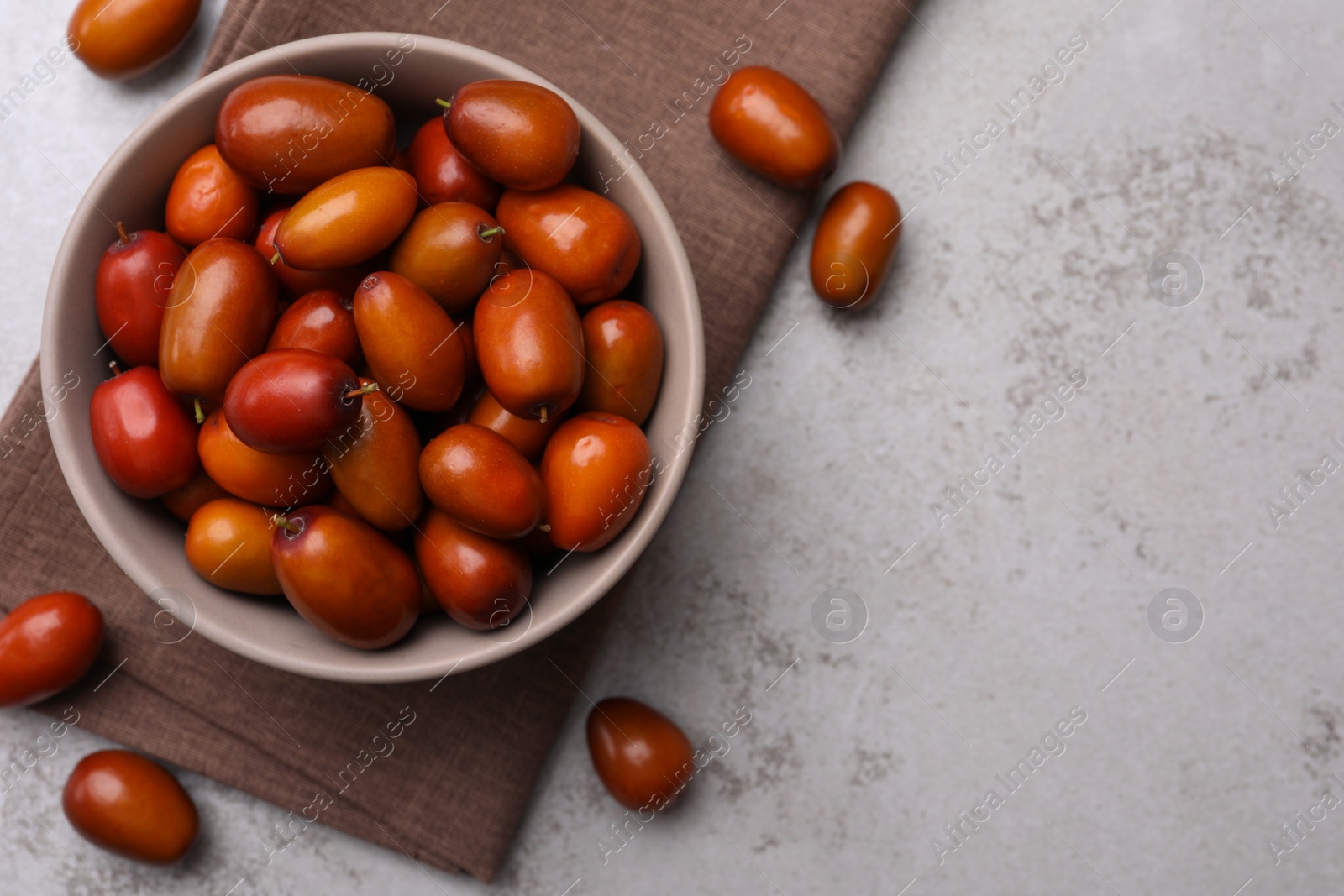 Photo of Fresh Ziziphus jujuba fruits with bowl and napkin on light table, flat lay. Space for text