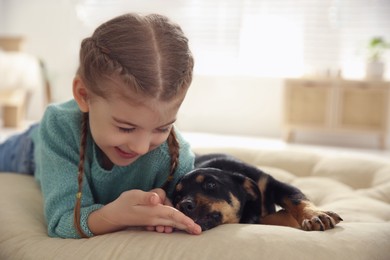 Photo of Little girl with cute puppy lying on soft pillow at home