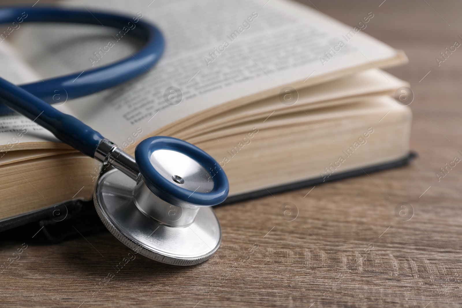 Photo of Student textbook and stethoscope on wooden table, closeup. Medical education