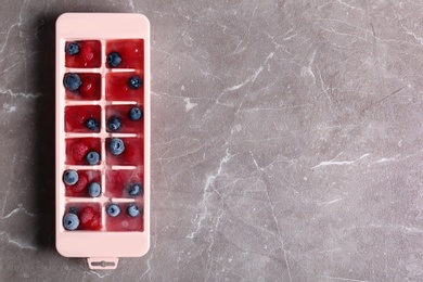 Ice cubes with berries in tray on table, top view. Space for text