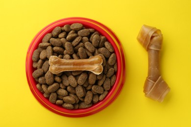 Chew bones and dry dog food on yellow background, flat lay