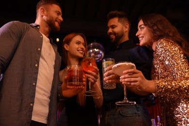 Photo of Happy friends holding glasses with fresh cocktails in bar, low angle view