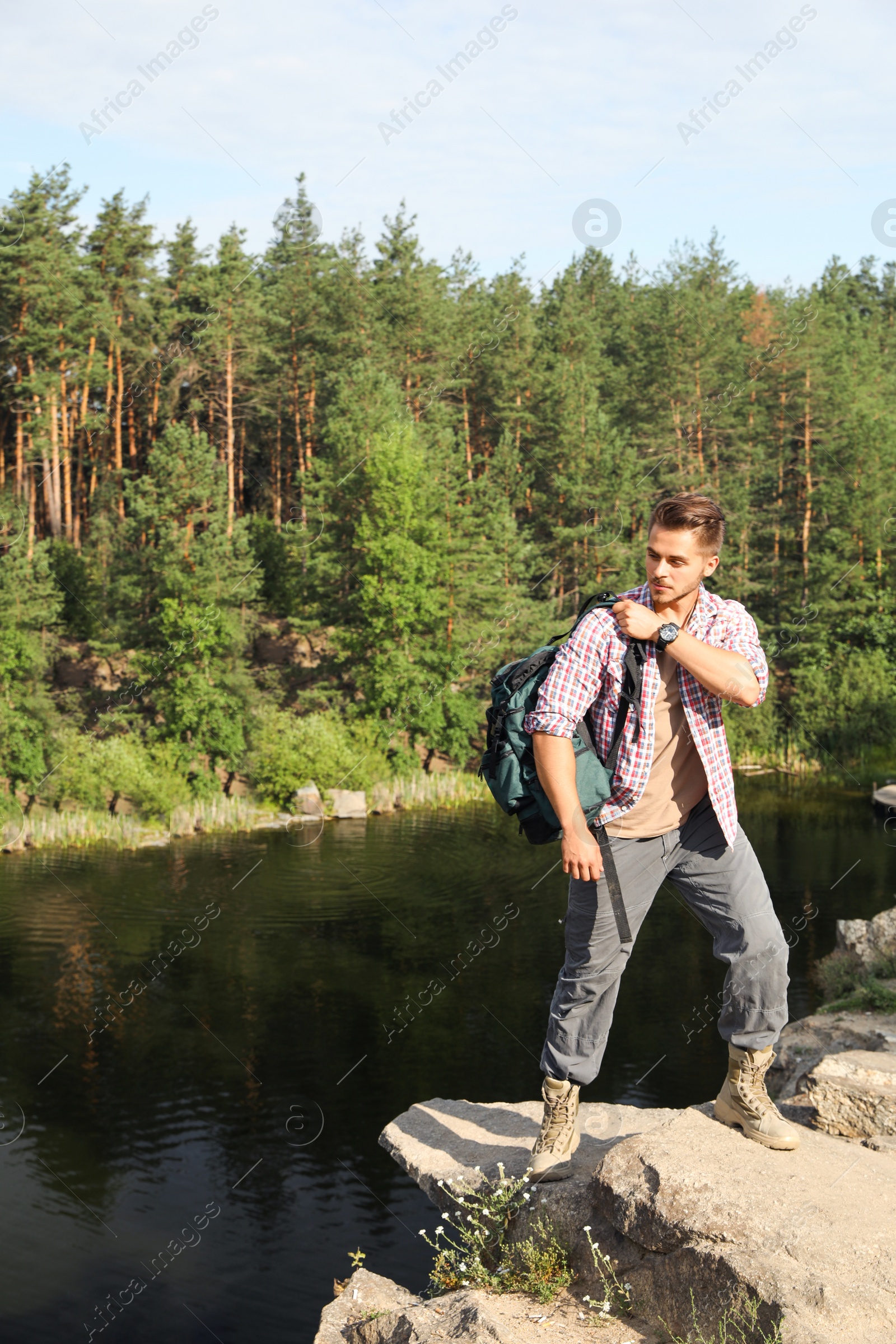 Photo of Young man on rock near lake and forest. Camping season