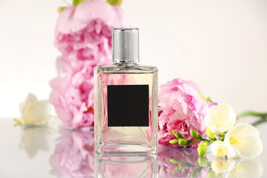 Photo of Bottle of luxury perfume and floral decor on mirror surface against white background