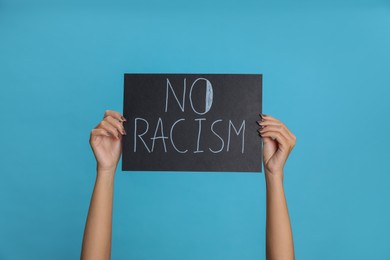 Photo of Woman holding sign with phrase No Racism on light blue background, closeup