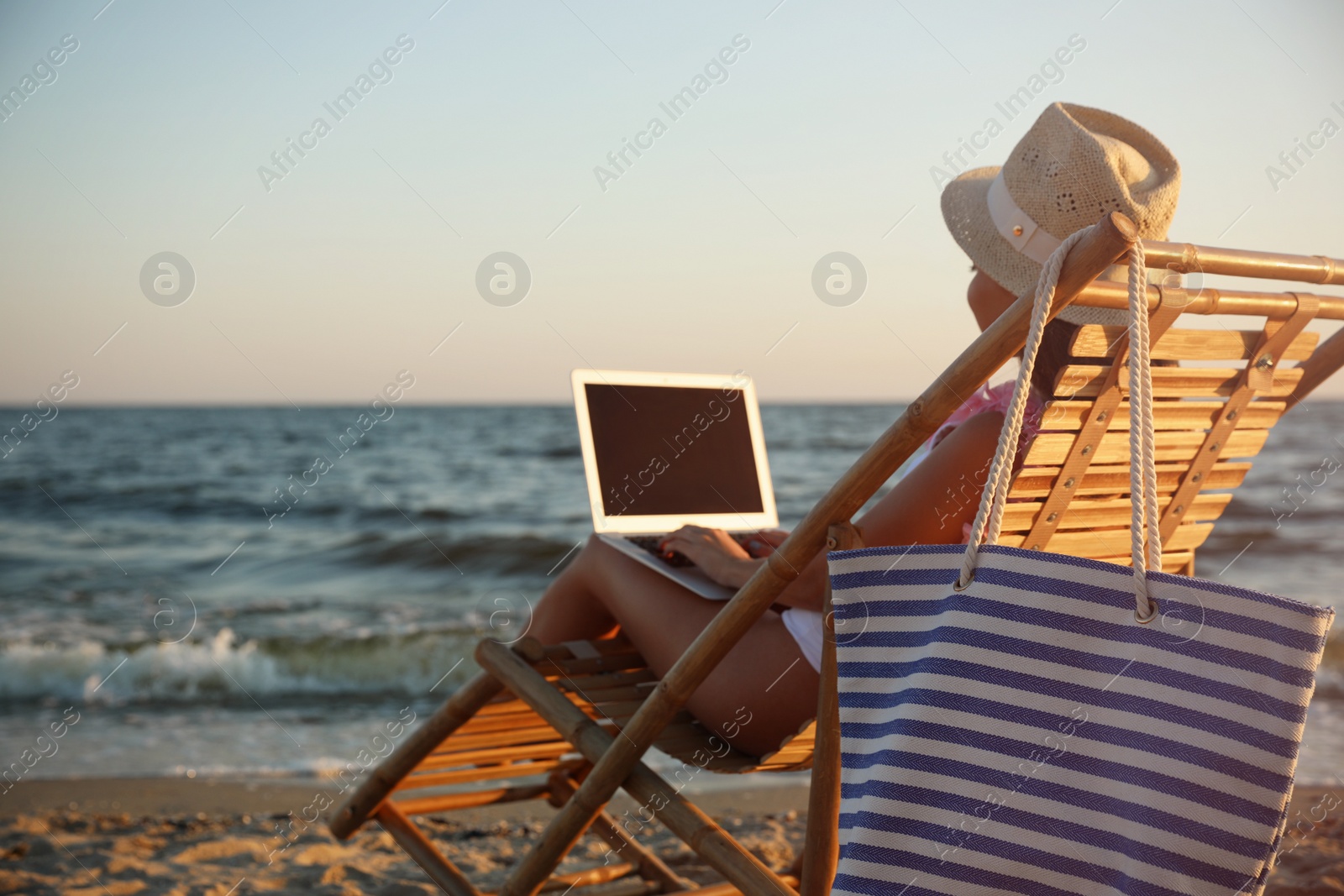 Photo of Young woman with laptop in deck chair on beach