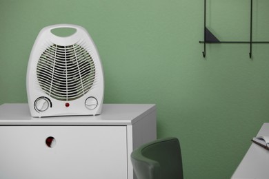 Photo of Modern electric fan heater on chest of drawers indoors. Space for text