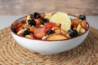 Photo of Bowl with mixed dried fruits and nuts on wicker mat, closeup
