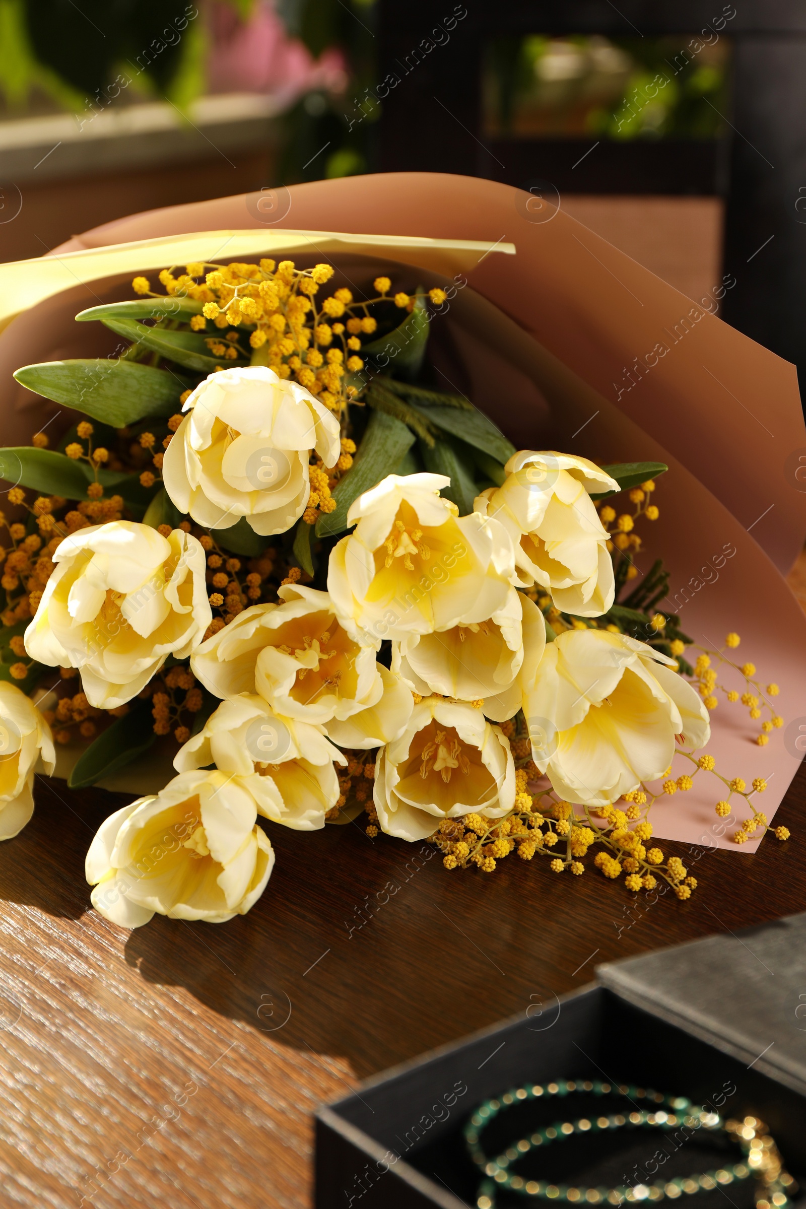 Photo of Bouquet with beautiful tulips, mimosa flowers and box of jewelry on wooden table indoors