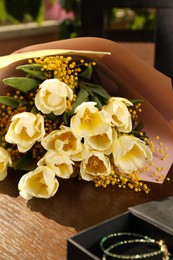 Bouquet with beautiful tulips, mimosa flowers and box of jewelry on wooden table indoors