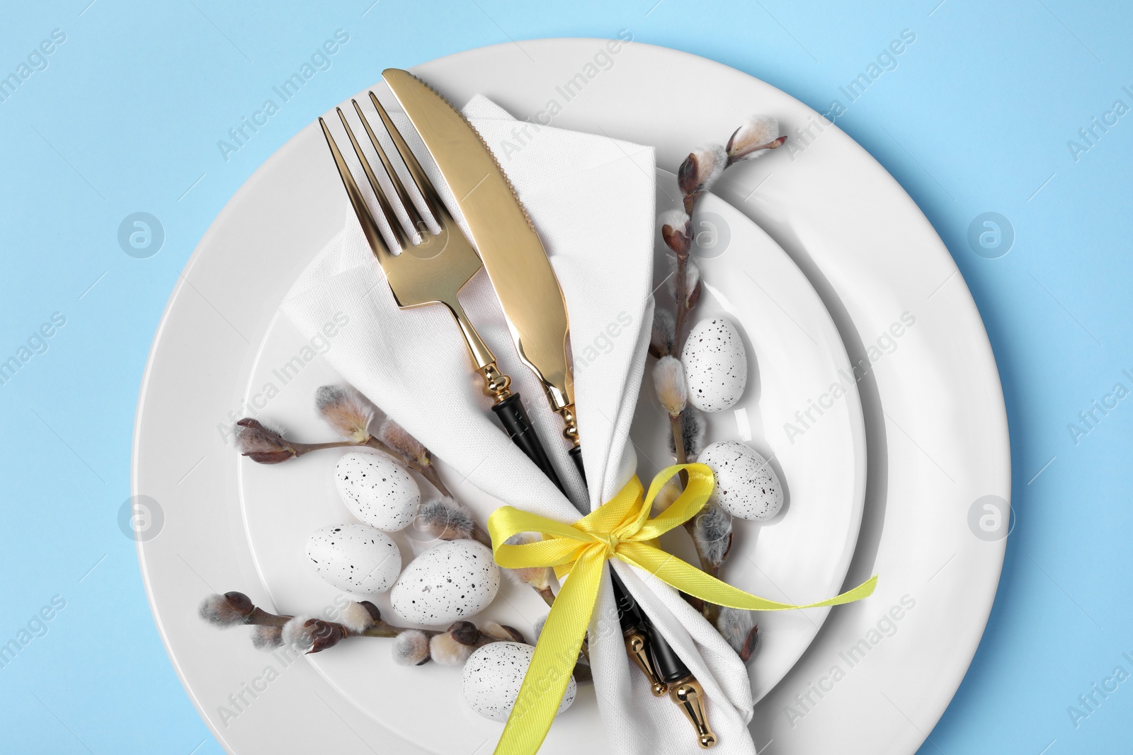 Photo of Festive table setting with willow twigs on light blue background, top view. Easter celebration