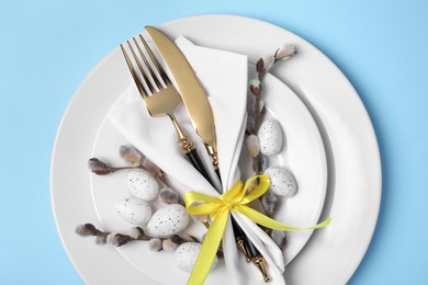Festive table setting with willow twigs on light blue background, top view. Easter celebration