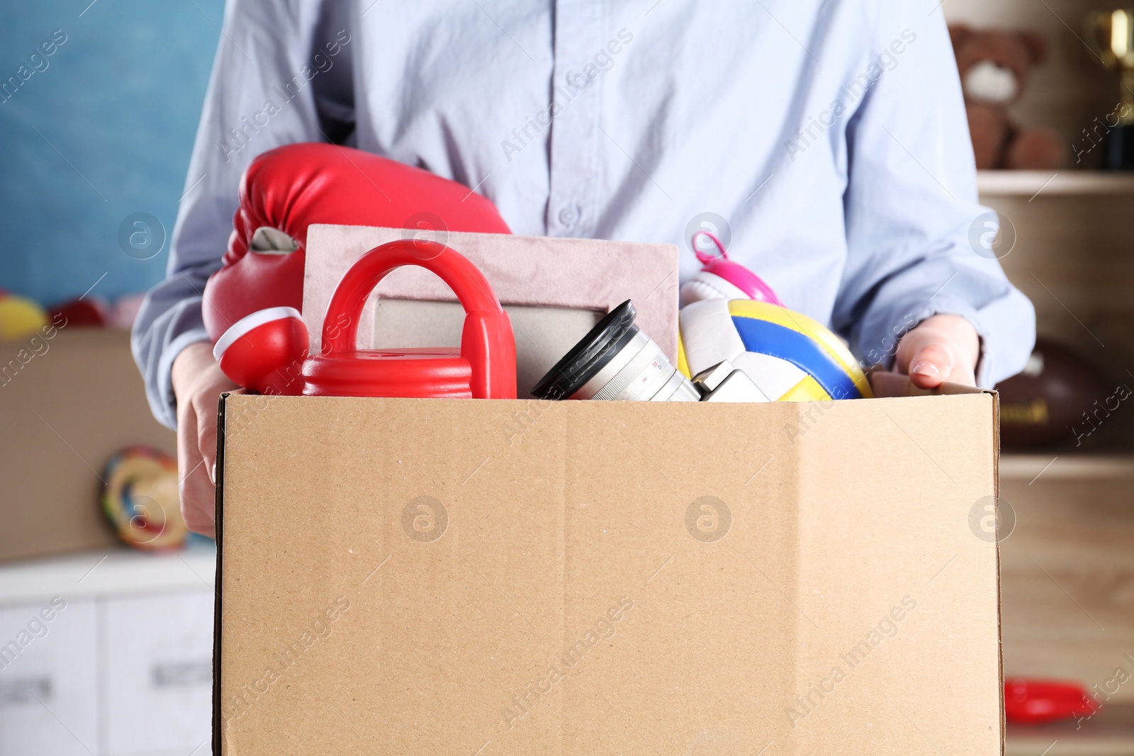 Photo of Woman holding box of unwanted stuff indoors, closeup