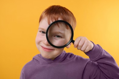 Photo of Boy looking through magnifier glass on yellow background