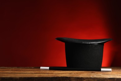 Photo of Magician's hat and wand on wooden table against red background, space for text