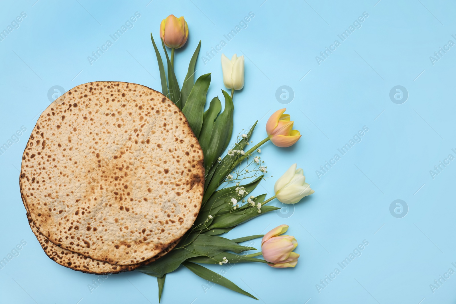 Photo of Tasty matzos and fresh flowers on light blue background, flat lay. Passover (Pesach) celebration