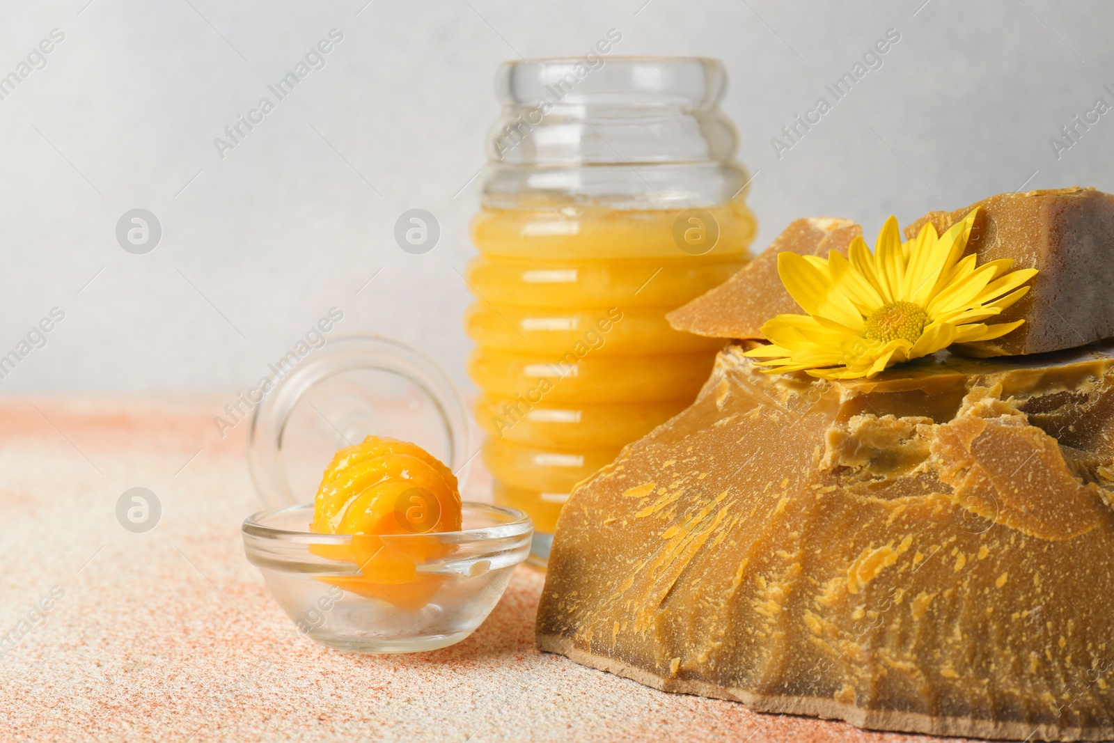 Photo of Natural beeswax blocks, flower and jar of honey on color textured table, closeup. Space for text