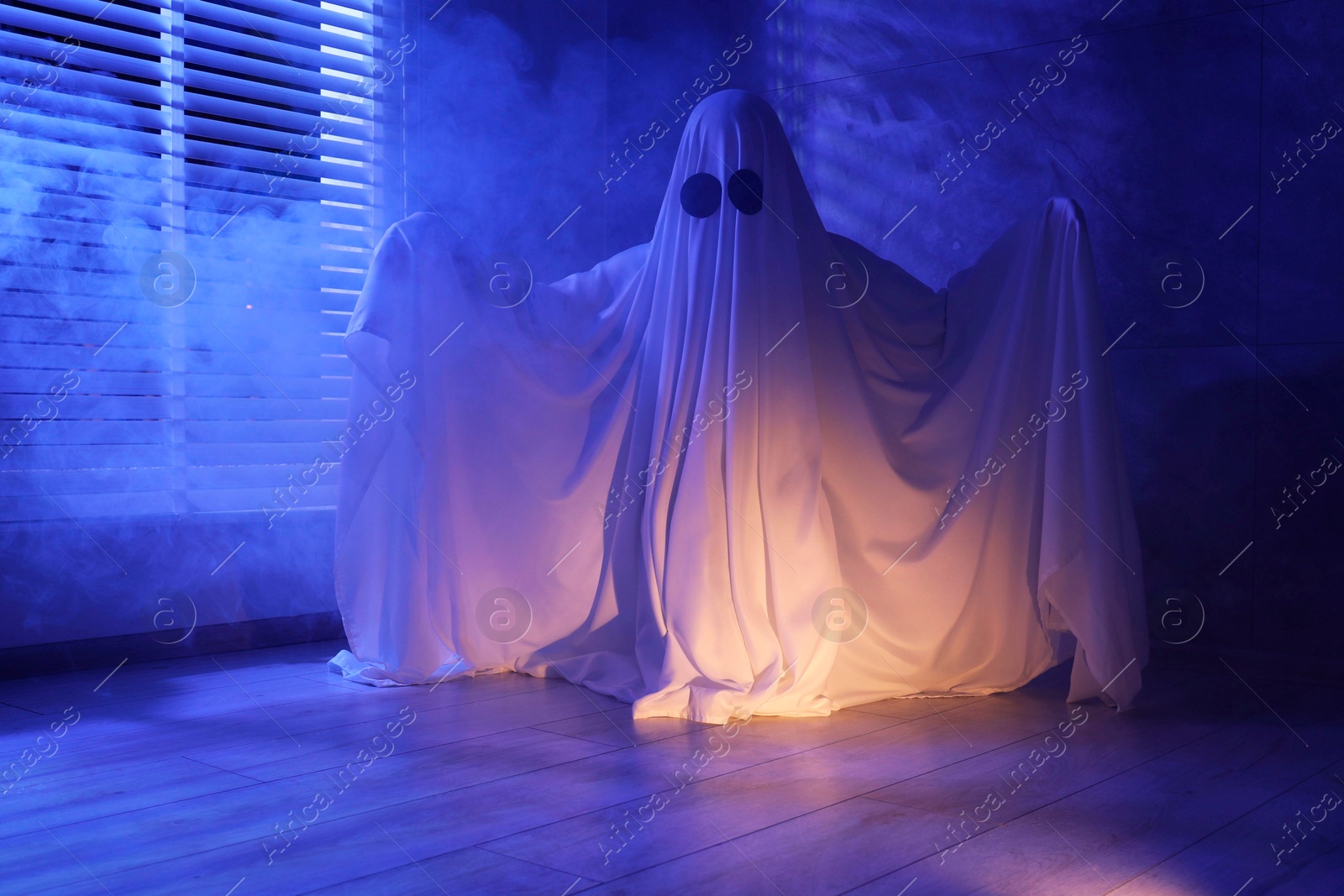 Photo of Creepy ghost. Woman covered with sheet near window in blue light