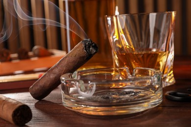 Photo of Cigars, ashtray, whiskey and cutter on wooden table, closeup