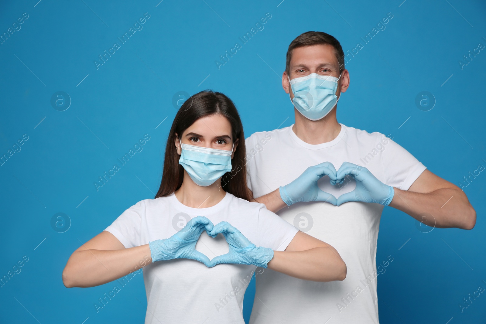 Photo of Volunteers in protective masks and gloves showing heart gestures on blue background. Aid during coronavirus quarantine