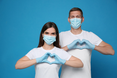 Photo of Volunteers in protective masks and gloves showing heart gestures on blue background. Aid during coronavirus quarantine