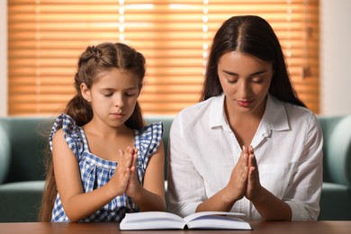 Photo of Young woman with her little daughter praying together over Bible at home